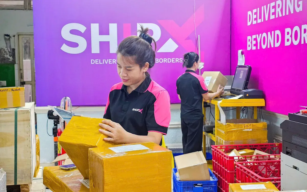 ShipX warehouse staff packing parcels in front of the ShipX "Delivering Beyond Borders" wall.